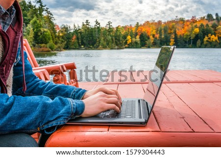 Work from anywhere - working on laptop beneath the autumn sky while on a deck near the water's edge. concept - background