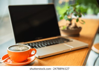 Work area with laptop Orange coffee with latte art and small potted plants The focus is on the coffee cup. with a laptop and trees in the background In a coffee shop or home office - Powered by Shutterstock