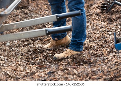 Work Boots Standing In Leaves Near A Wheel Barrow.