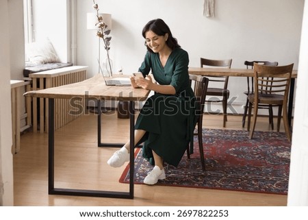 Work break for texting. Smiling relaxed millennial female freelancer take pause from notebook tasks at shared workspace desk text message on cellphone chat with friend colleague browse social media