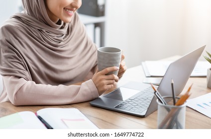 Work With Comfort. Cropped Image Of Muslim Woman In Hijab Drinking Coffee At Desk And Working On Laptop In Office