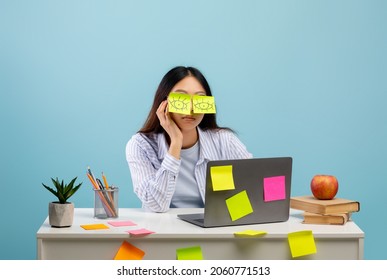 A lot of work concept. Tired asian female student sleeping with stickers on eyes, sitting at table over blue studio background. Distracted woman at home office