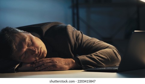 Work Deadline. Sleeping Man. Office Stress. Exhausted Guy Laying Head On Desk Falling Asleep Late Dark Room Interior.