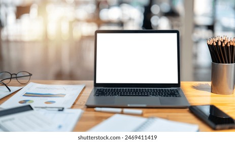 Work desk with a modern laptop featuring a blank screen, flanked by business charts, glasses, and office supplies in a bright workspace.

 - Powered by Shutterstock