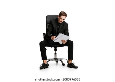 Work With Documents. Portrait Of Young Man In Black Business Suit, Office Manager Sitting On Chair Isolated On White Background. Art, Inspiration And Ad Concept. Businness, Modern Mobile Lifestyle