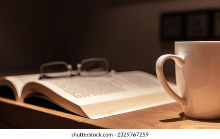 Work environment at night, open book, glasses and coffee under lights