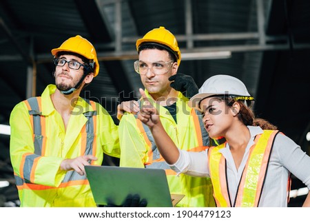 Work at factory. workers man and engineer woman team working together in safety work wear with white and yellow helmet using laptop computer.professional women engineer pointing in factory meeting
