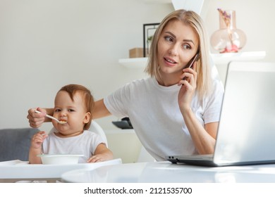 Work from home. Business mother is talking on phone while sitting at table with a laptop and feeding her little daughter. Motherhood, maternity, childhood and care concept. - Shutterstock ID 2121535700