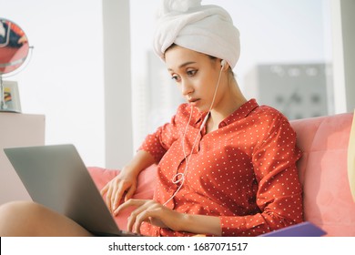 Work from home concept - Beautiful young woman in red pajamas shirt and bath towel head wrap working on laptop, listen to music with earphones. Working at home. Quarantine. - Powered by Shutterstock