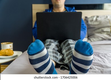 Work from home concept. Man dressed in a hoody and pijamas having a conference call on a bed with a laptop.