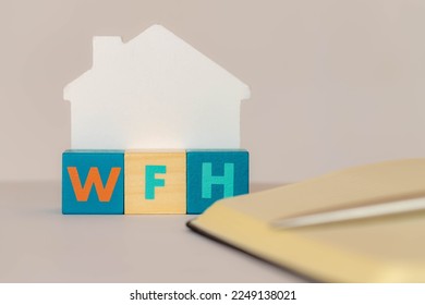 Work from home concept, Selective focus of colourful wooden blocks alphabet with abbreviations word WFH, Multicolour wood cube and notebook on white background, Free copyscape for your text.