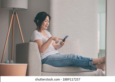 Work From Home Happy Asian Mature Woman Relaxing In Sofa Using Mobile Phone Online Shopping Or Remote Working.