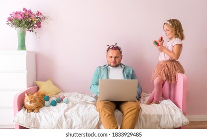 Work From Home. Kid Disturbing Dad Working Remotely Because Of Covid. Funny Child Girl Putting On Make Up And Make Hair Style. Man Working On Pink Bed With Laptop In Girls Room Interior.