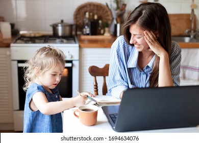 Work From Home Office With Kid. Working Mother Using Laptop. Cozy Freelance Workplace At Kitchen Table. Happy Female Business, Woman Career. Cute Child Drawing In Mom Notebook. Lifestyle Family Moment