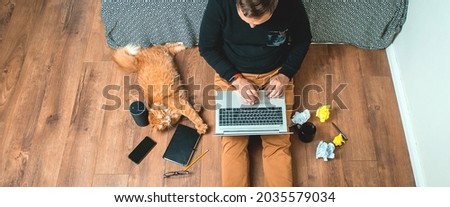 Work from home on creative workspace. Man sitting on floor with laptop computer and smart speaker. Ginger pet cat lying. Home office. Remote work.