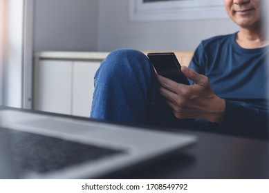 Work From Home, Teleworking, Internet Technology Concept. Happy Asian Casual Business Man, Freelancer Chilling Using Mobile Smart Phone, Working On Laptop Computer Browsing Internet At Home Office