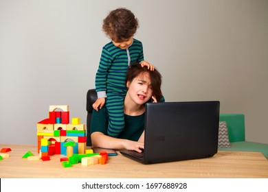 work at home. tired woman with a child on his neck sitting at a computer and talking on the phone with the employer while the child is playing cubes and hanging around her. inability to work at home.