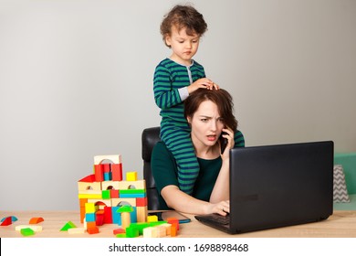 work at home. tired woman with a child on his neck sitting at a computer and talking on the phone with the employer while the child is playing cubes and hanging around her. inability to work at home.