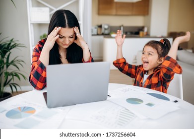 Work At Home. Tired Young Mom Try To Work Remotely On Laptop At Home, And Her Cute Funny Daughter Interferes With Her And Distracts