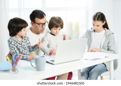 Work at home together. Caring latin father using laptop, working from home and watching kids drawing while sitting at the table with him