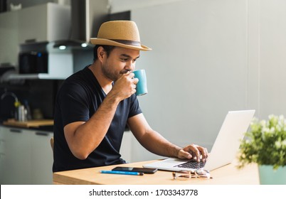 Work From Home Of Young Asian Man Holding And Drinking A Cup Of Coffee In The Morning. Casual Asian Businessman Age Around 30 Using On Laptop For His Work.