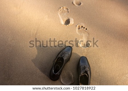 Work Life Balance Concept, Businessman take off his Working Oxford Shoes and leave it on the Sand Beach for Walk into the Sea on Sunny Day. Top View