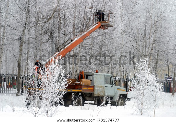 Work on the\
aerial work platform. He hangs a garland, bulbs on the branches of\
trees covered with white frost, snow. Winter holiday background.\
Preparation for the New\
Year