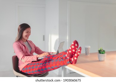 Work online remote from home funny concept. Asian woman relaxing in pajama pants and cozy socks while wearing professional top and suit for videocall meeting on WFH.