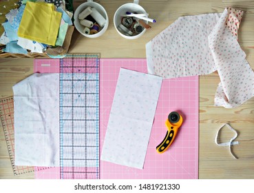 Work Place: Cotton Fabrics, Pink Cutting Mat, Quilting Ruler, Rottary Cutter, Sewing Supplies In White Cups And Wooden Desk