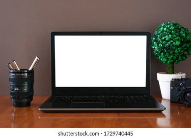 Work Place - Retro Camera, Mug With Pens And Open Laptop With Mockup On Screen. Wooden Table And Green Plant. Background Brown Wall.