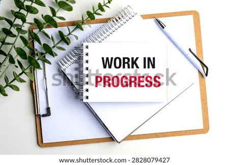 Work in progress concept displayed on notebook with clipboard, pen and green plant on modern office workspace . 
