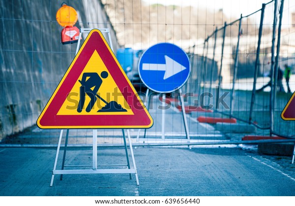 Work in\
progress. Roadworks, road signs. Men at work. Some signs signage\
for work in progress on urban street. Barriers and road signs.\
Silhouette of a worker at work. Right\
arrow.