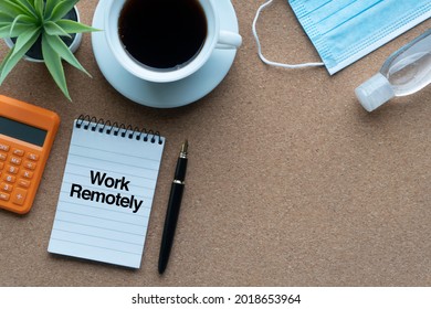 WORK REMOTELY text with calculator, notepad, hand sanitizer, decorative plant, coffee cups and fountain pen on wooden background. Technology, Business and copy space concept