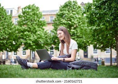 Work remotely. A woman takes online courses in the park, sitting on the lawn. The concept of a remote office. The girl looks at the laptop sitting on the lawn. - Shutterstock ID 2160162721