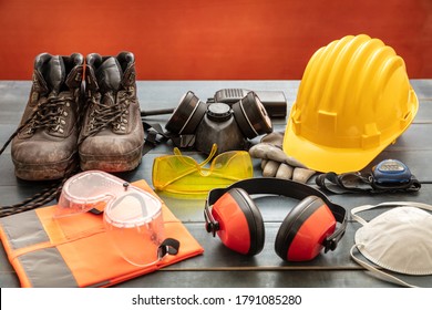 Arbeitsschutzausrüstung. Industrielle Schutzausrüstung auf Holztisch, roter Hintergrund. Sicherheitskonzept für Baustellen