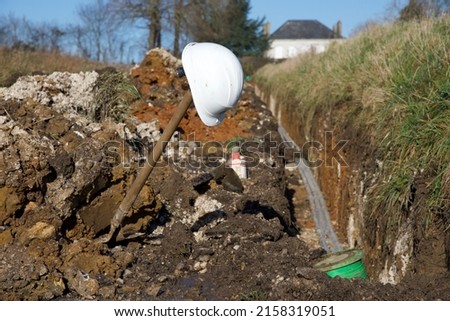 Work site: in the process of burying roadside tubes to carry fibre optic cables a workman's hard hat rests atop his shovel's handle.
