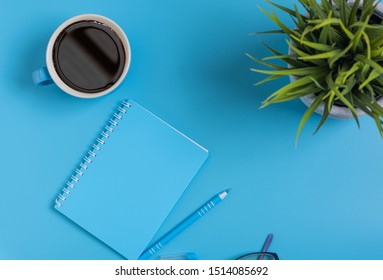 Work Space Blue Set Of Note Pad,pen,eyeglasses And Coffee Cup On Blue Desk Background,top View