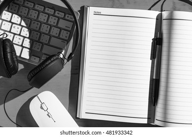 Work space desk with open notebook and pen, keyboard, mouse and headphone, Black and white toned