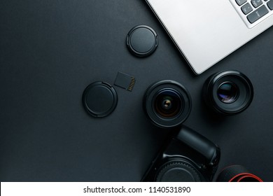 Work space on black table of photographer. Minimal workspace with Laptop, camera and lens copy space on dark background. Modern and elegant. Top view. Flat lay style.