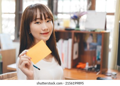 Work And Study Online From Home WFH Office Concept. Portrait Of Young Asian Cute Student Teenager Woman Hold A Note Paper For Remind. Eye Looking At Camera