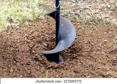 Work Tool. A Large Black Drill Rotates. He Is Drilling A Hole In The Ground. During Operation, Land Plots Fly In Different Directions. Blur Shows The Direction Of Flight Of Pieces Of Land. Blurred