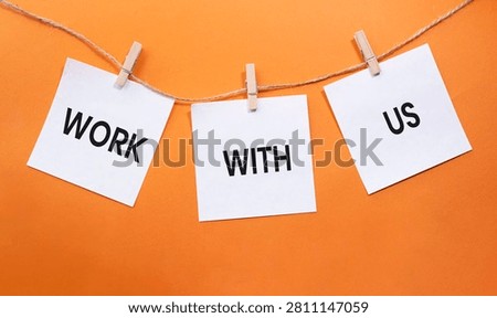 Work With Us text on white paper notes hanging on rope with clothespins over orange background. Recruitment, employment and career opportunity concept with copy space.