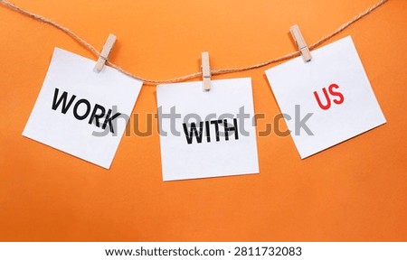 Work With Us text on white paper notes hanging on rope with clothespins over orange background. Recruitment, employment and career opportunity concept with copy space.