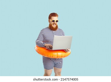 Work and vacation. Funny excited chubby man on pastel turquoise background working remotely with laptop during summer vacation. Red-bearded man in striped leotard with inflatable circle at waist.