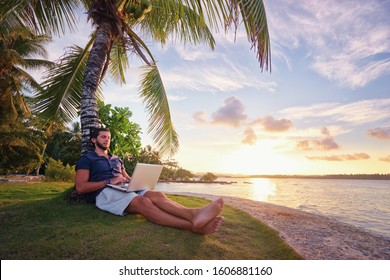 Work and vacation. Young man working on laptop computer on the tropical beach under the palm tree. - Powered by Shutterstock