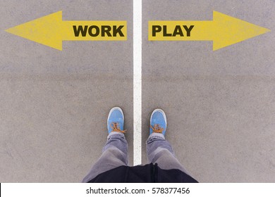 Work Vs Play Text On Yellow Arrows On Asphalt Ground, Feet And Shoes On Floor, Personal Perspective Footsie Concept