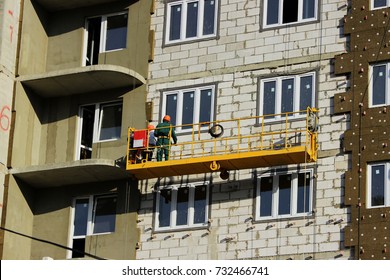 work with yellow front two suspended cradle with workers on a newly built high-rise building.
