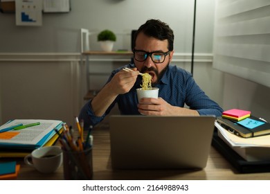 Workaholic Caucasian Man Eating Noodles Soup In Front Of The Computer While Working Late At The Office