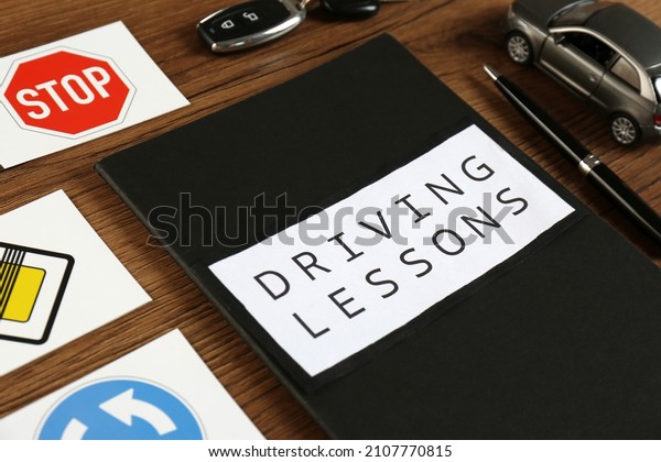 Workbook for driving lessons, pen\
and road signs on wooden table, closeup. Passing license\
exam