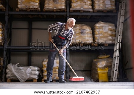 Workday in the factory. A senior factory worker is brooming factory hall.